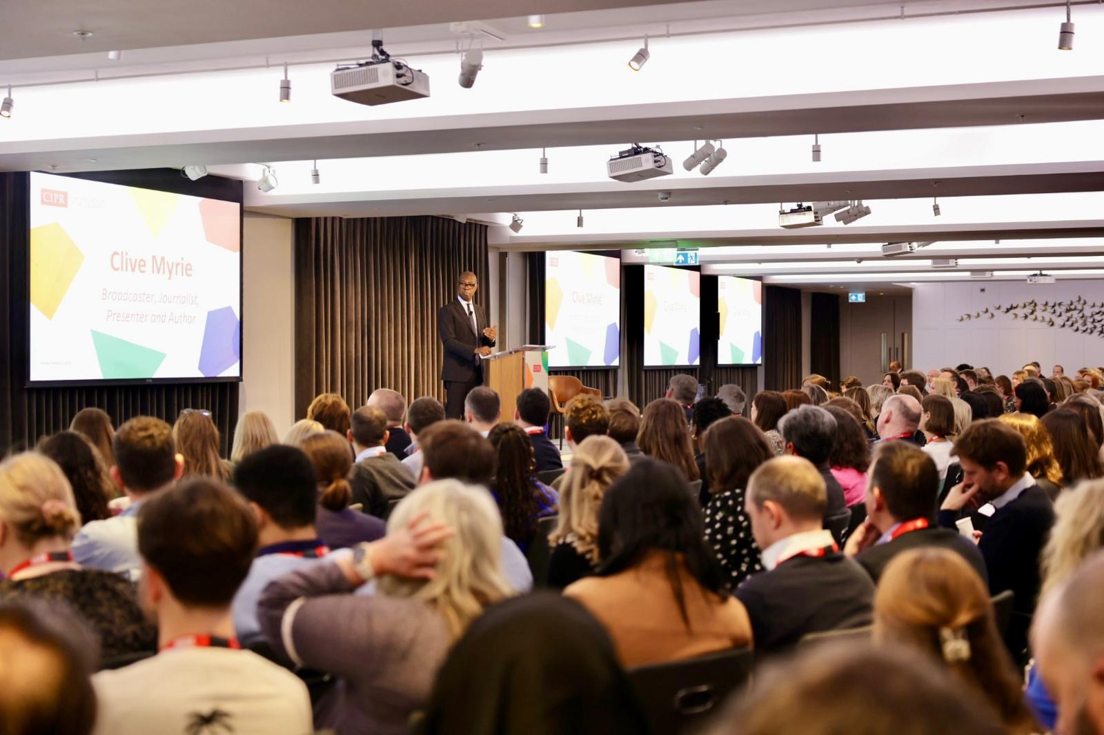 Clive Myrie, a broadcaster and journalist, stands at a podium addressing a large audience in at the CIPR’s 2024 ‘Changing Politics’ annual conference.
