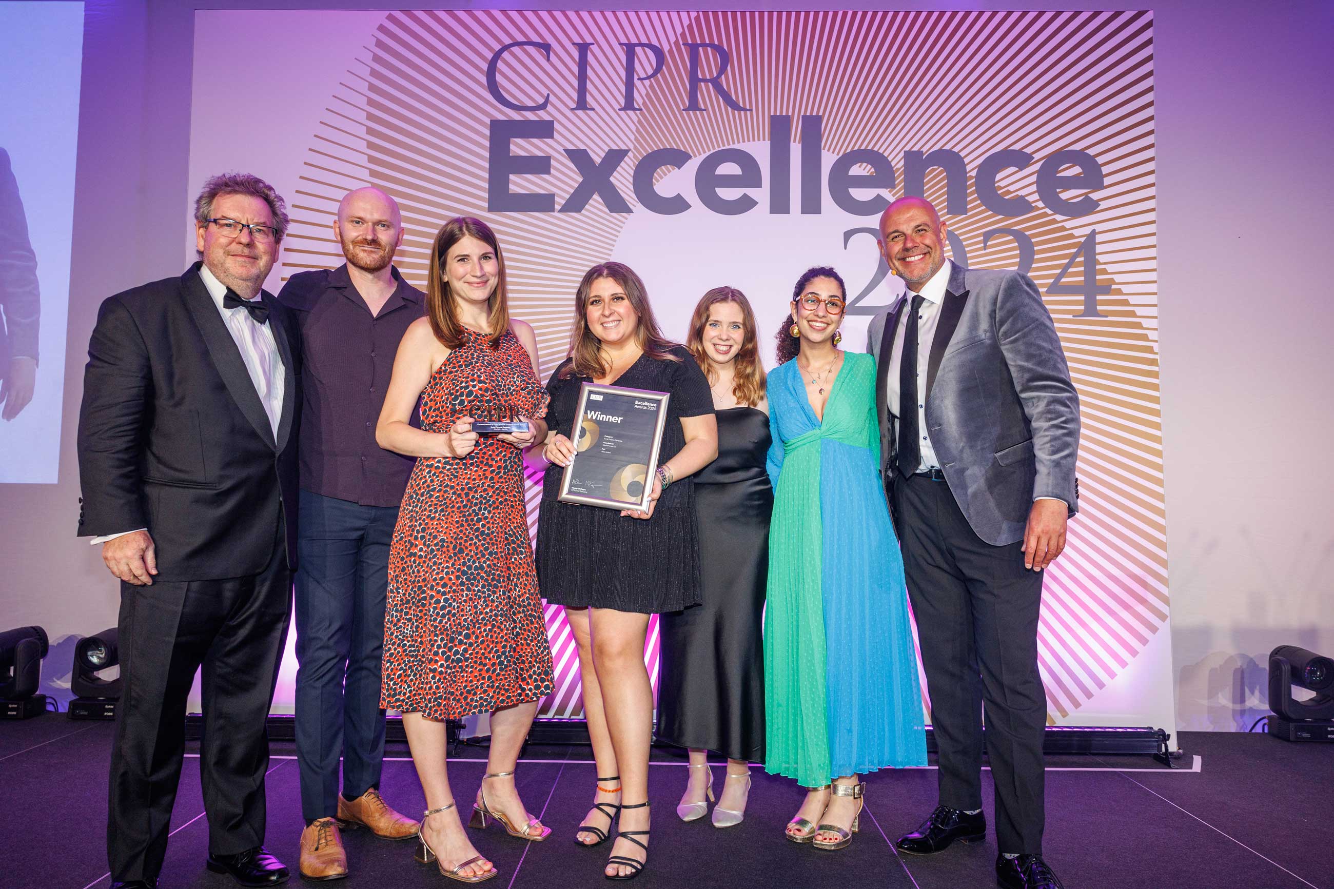 A group of CIPR Excellence awards winners posing on stage with their award.